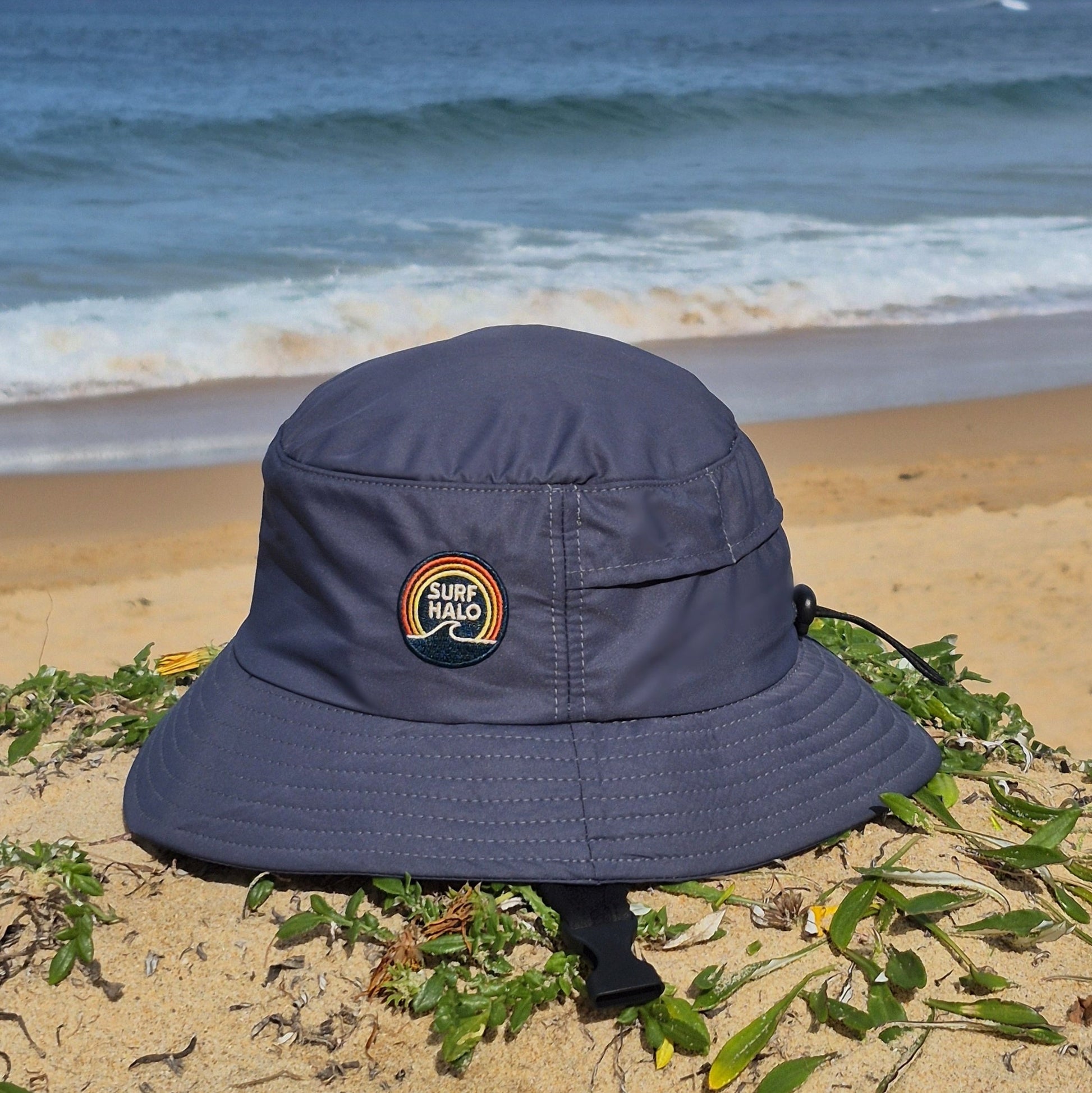 Surf hat charcoal bucket style wide brim UPF5+ adjustable back strap and chin strap in the beach side view