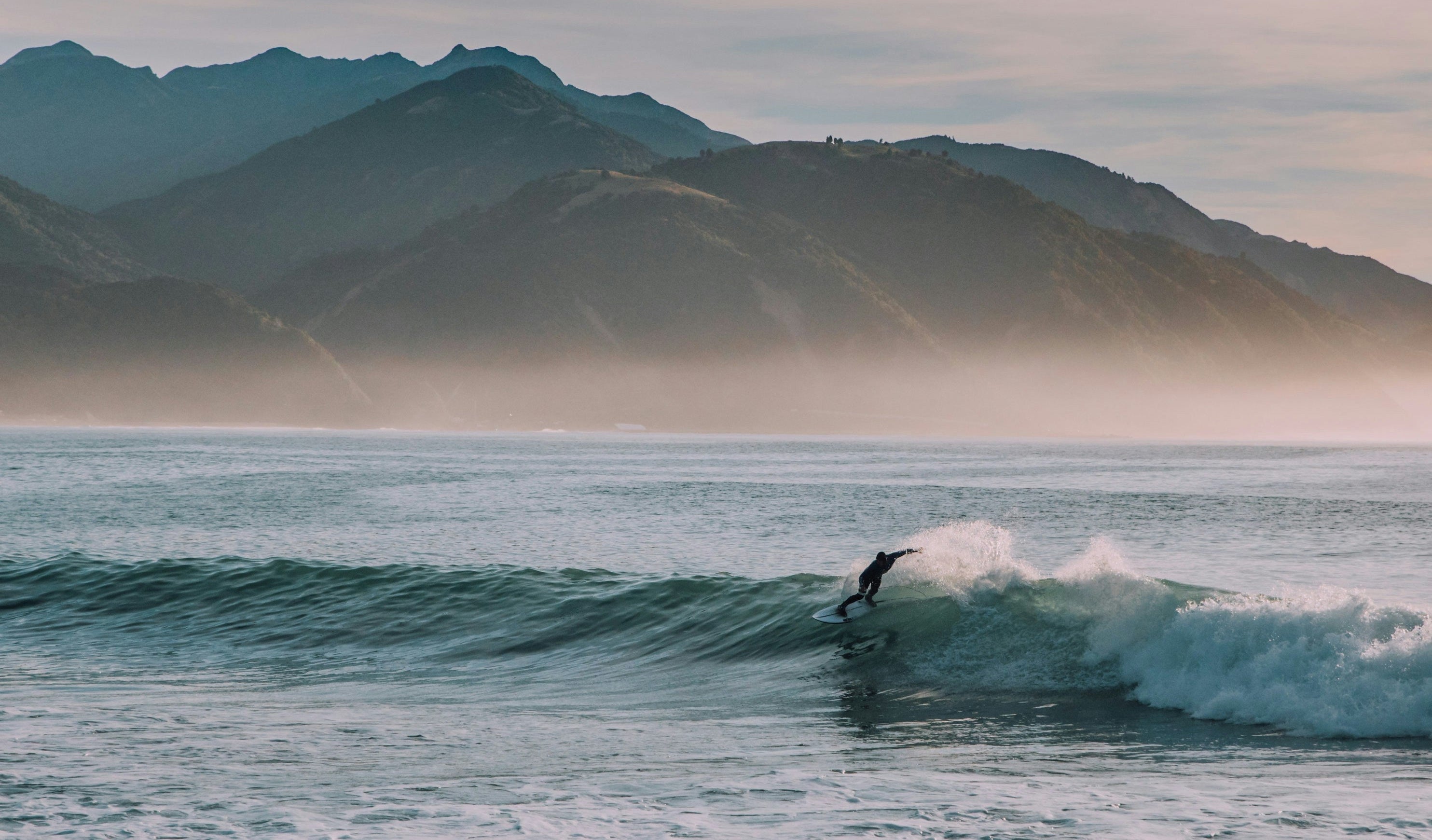 surfer riding a wave with mountains n the background