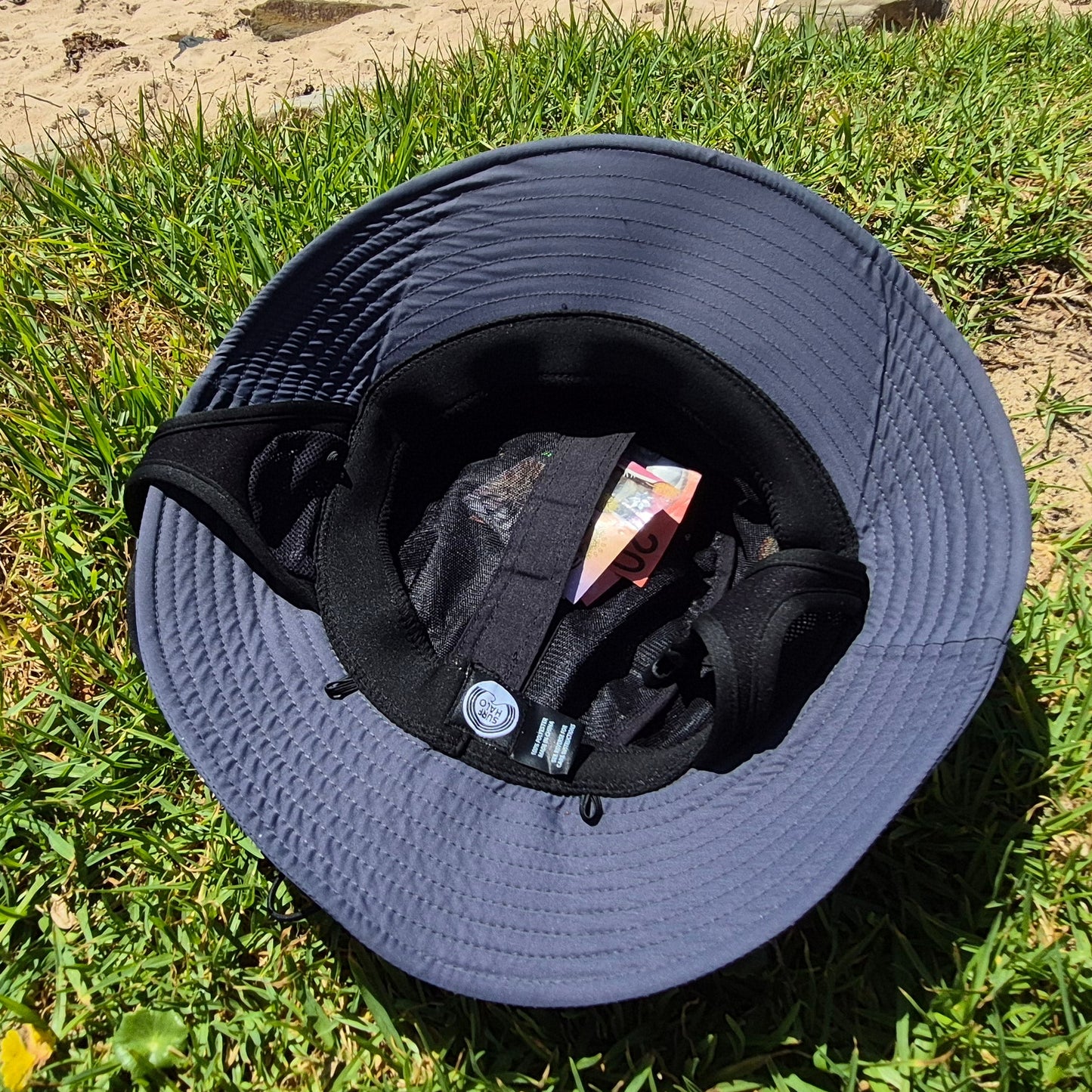 Grey surf hat on grass with a sandy background hidden pocket surf hat