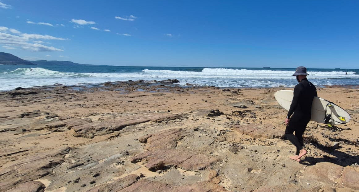 Person holding a surfboard on a rocky beach with ocean waves in the background