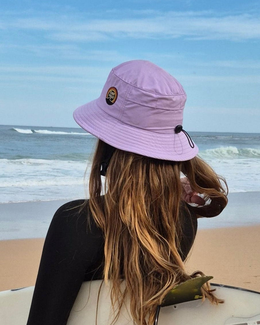 girl with a surf hat lilac holding a surfboard on the beach