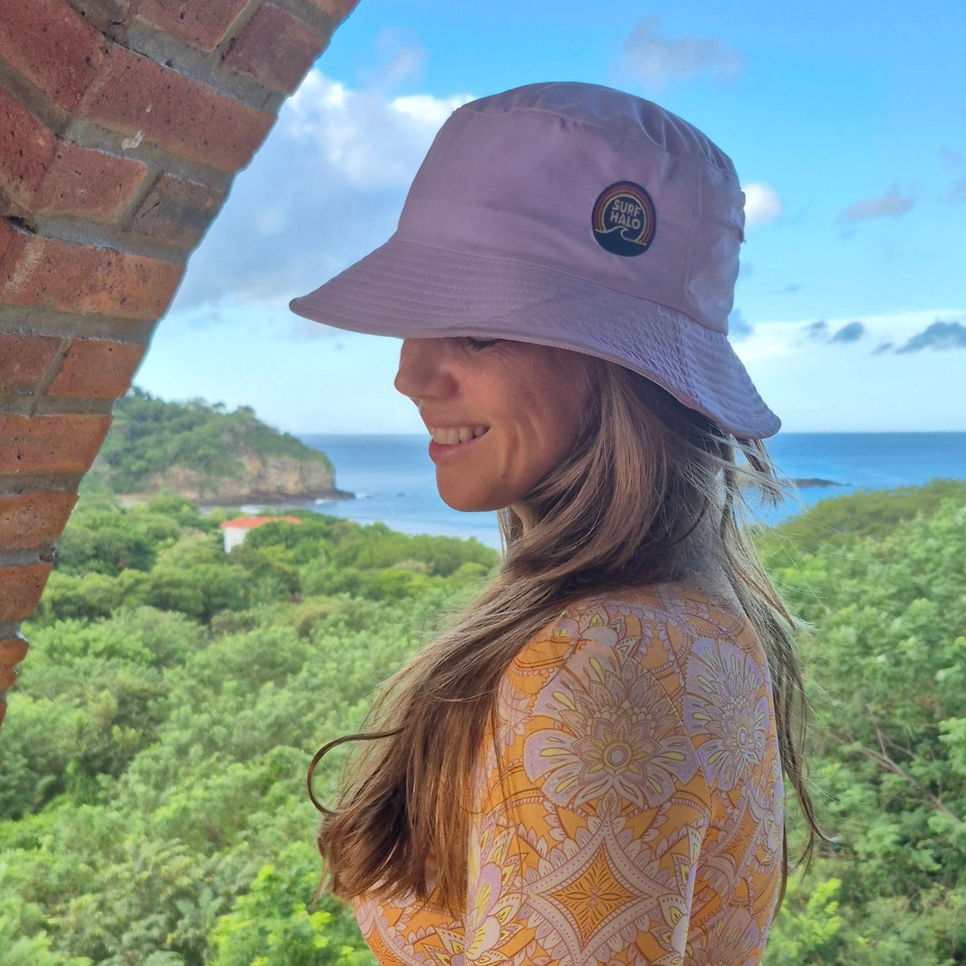 Woman wearing a lilac surf hat with ocean and mountains as background