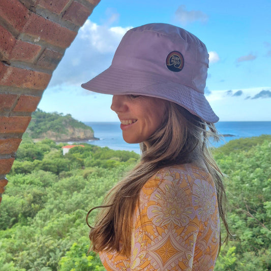 Woman wearing a lilac surf hat with ocean and mountains as background