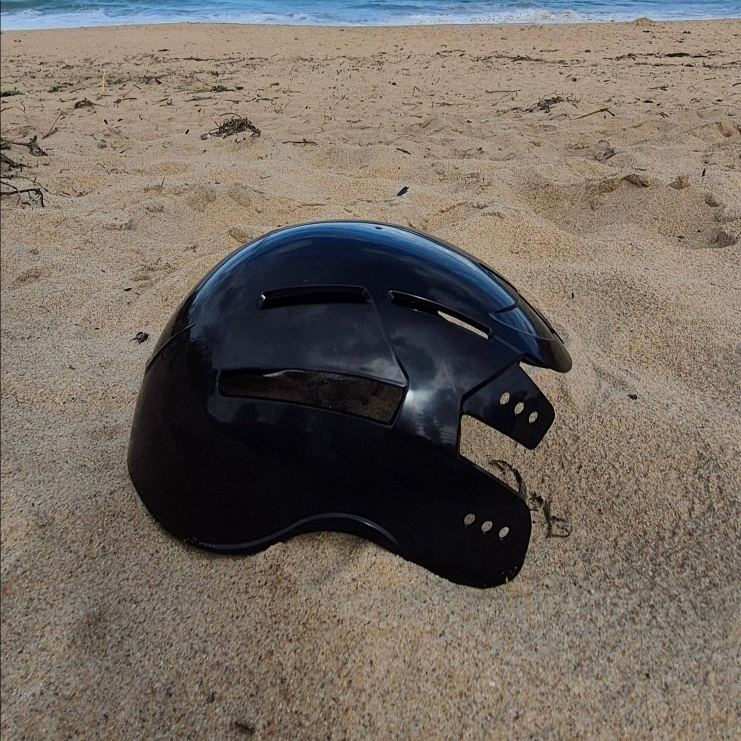 Black helmet on a sandy beach with ocean and blue sky in the background