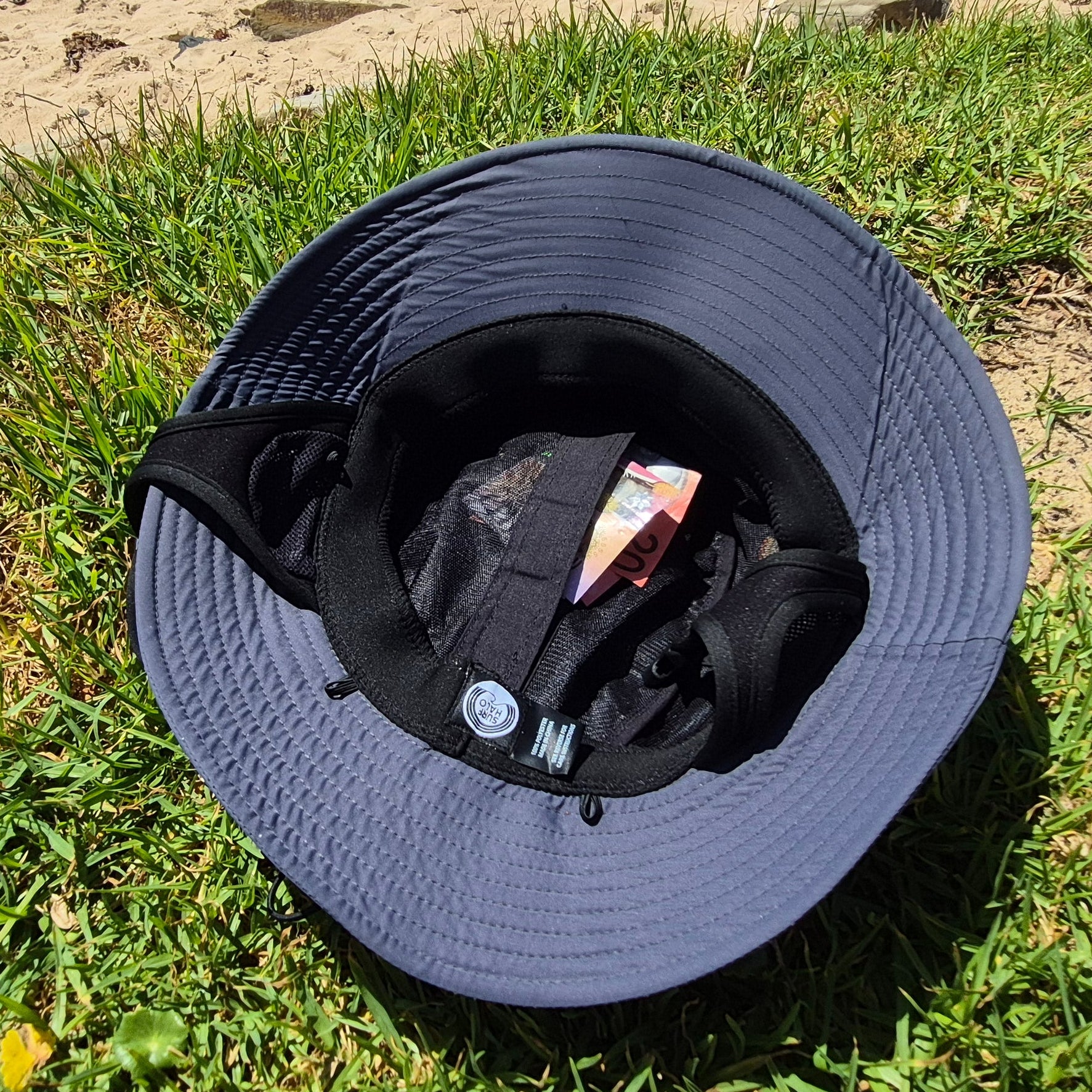 Grey surf hat on grass with a sandy background hidden pocket surf hat 