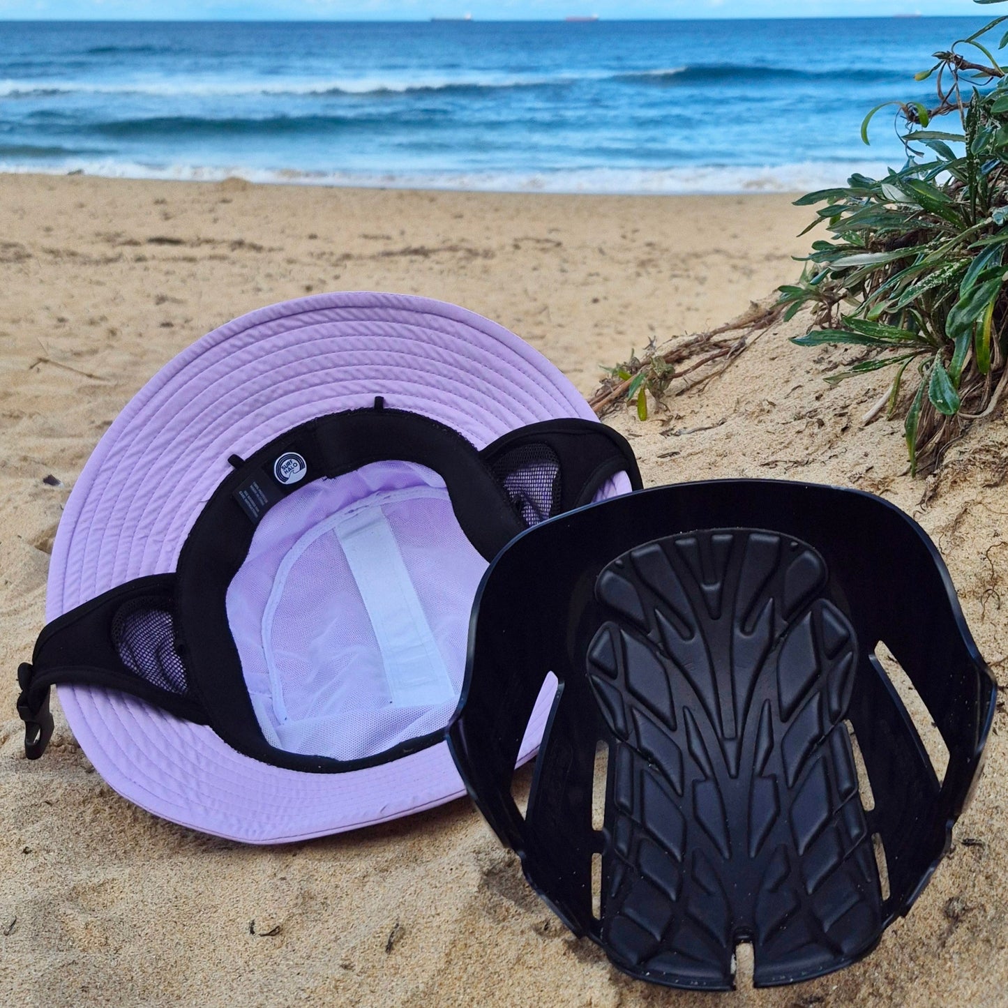 Lilac surf hat helmet internal view with the protective removable insert against bumps and cuts on a beach 