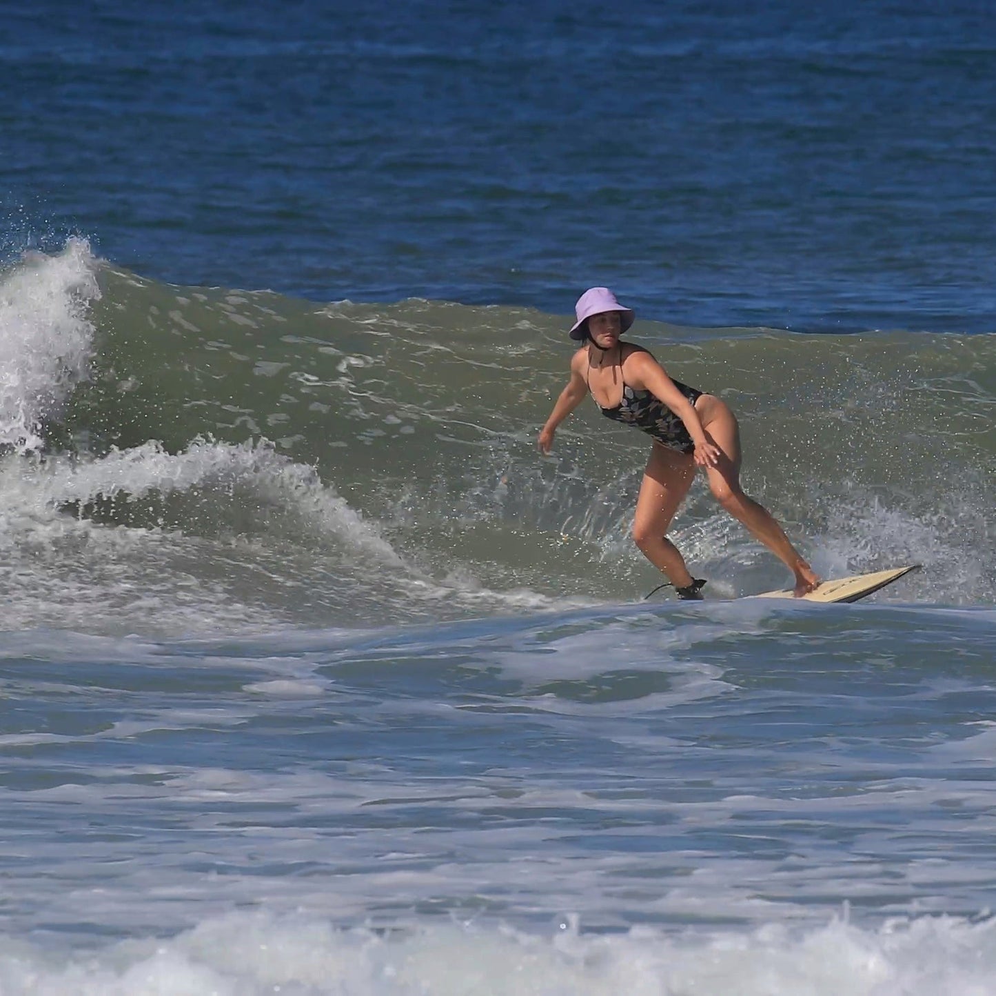 surfer girl on a wave wearing lilac surfing hat on a wave shortboard